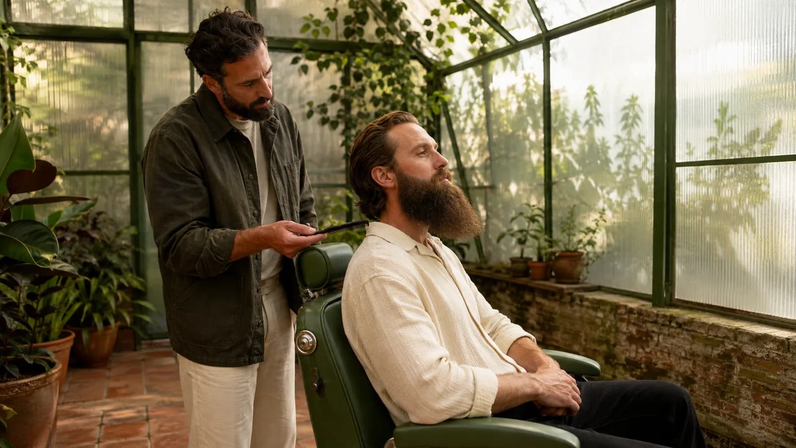 Adult man with a long beard and a barber examine the supportive underside with a comb in a greenhouse studio