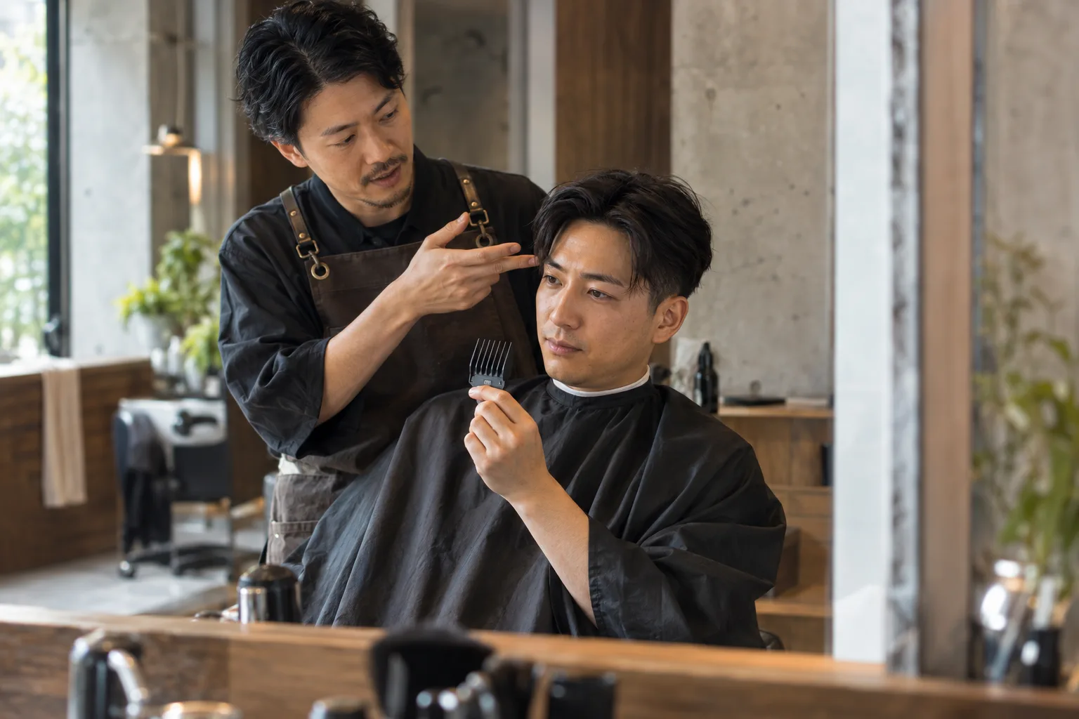 Adult client and barber discuss a buzz cut with a plain clipper guard in a warm studio