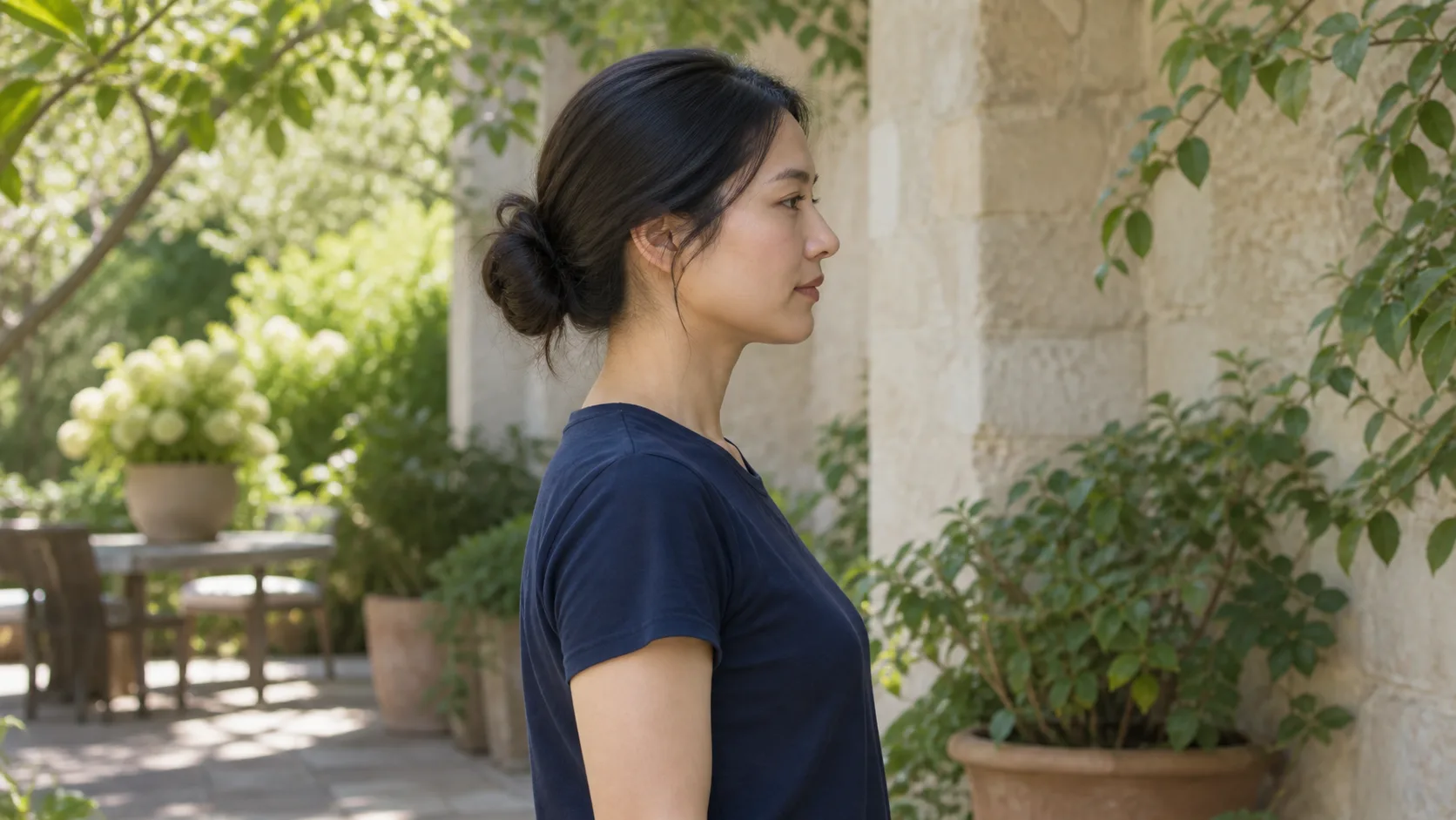 Adult woman turns in a calm true side profile against a shaded garden wall, with a natural chin position