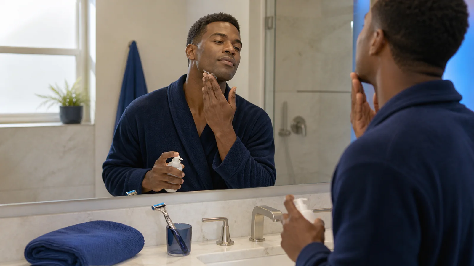 Adult man applying moisturizer to his freshly shaved jaw in a bright bathroom mirror